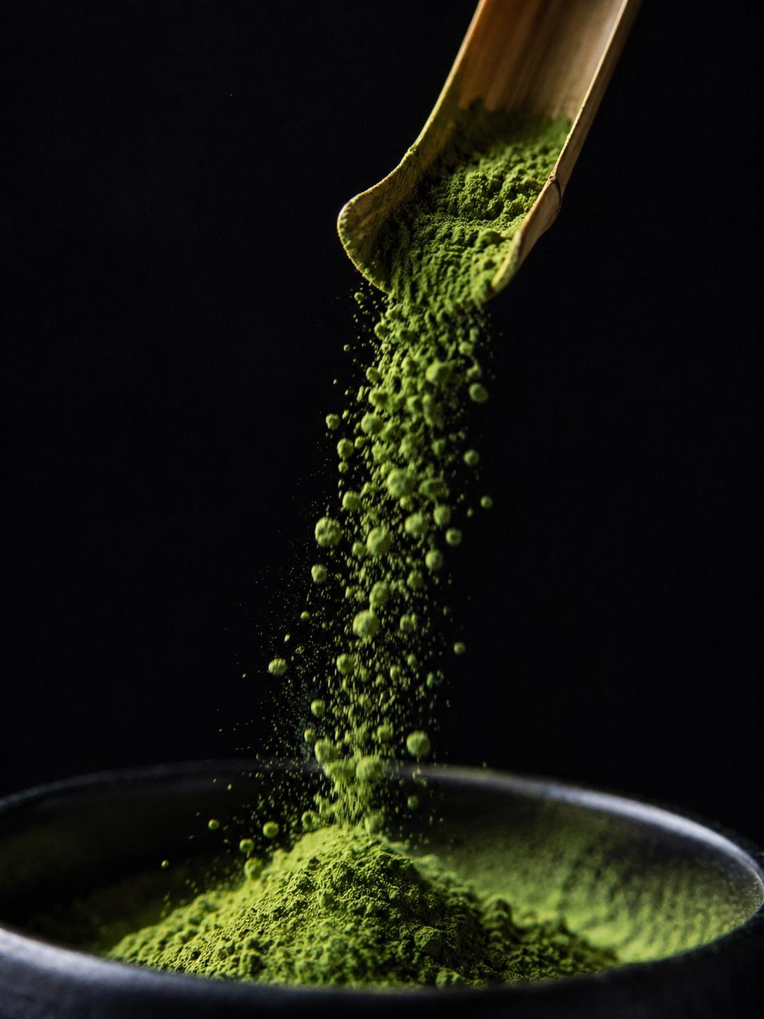 Emerald matcha powder cascading from a bamboo spoon on a dark background