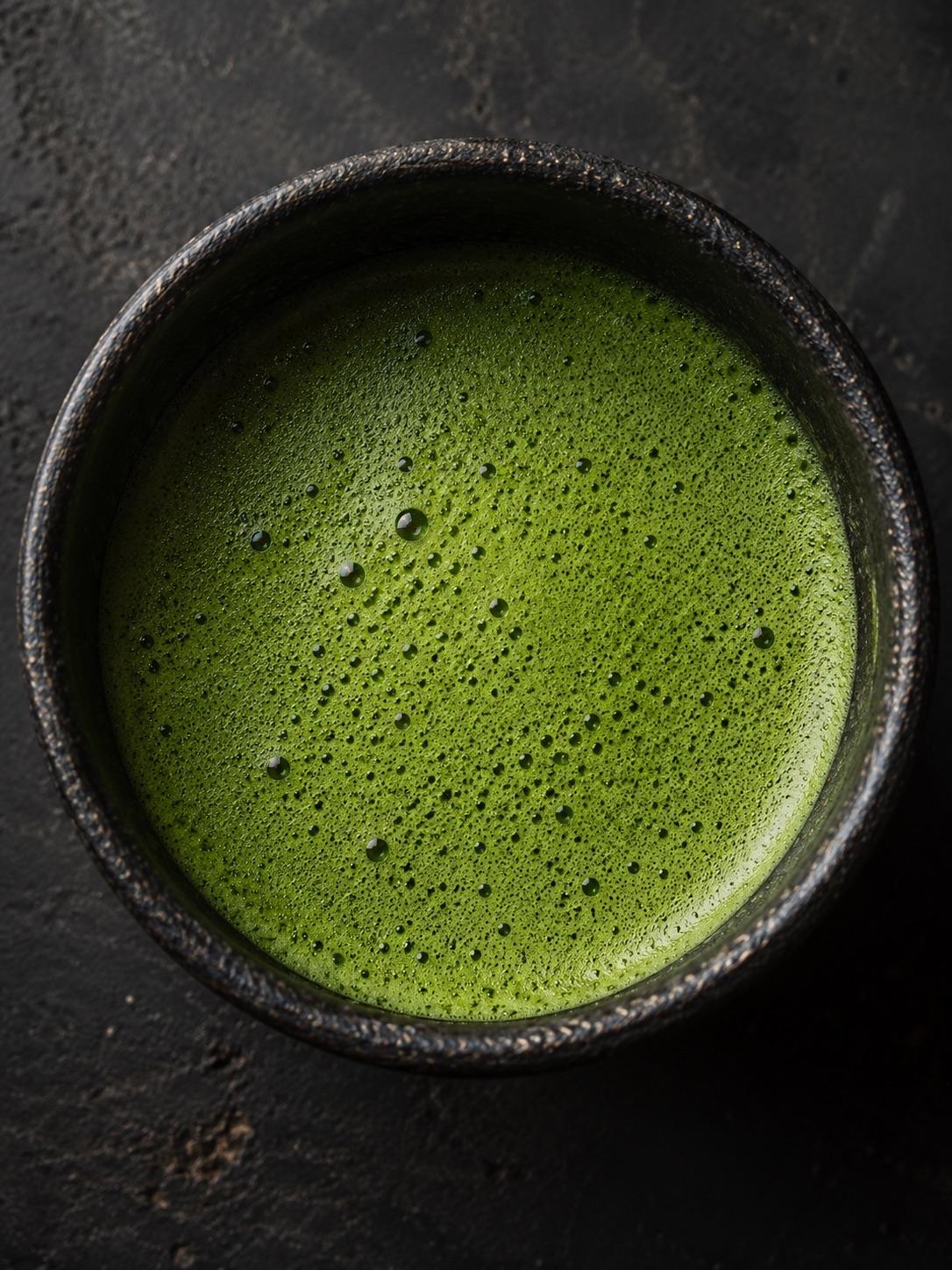 Top down view of frothy green matcha surface in a dark stoneware bowl